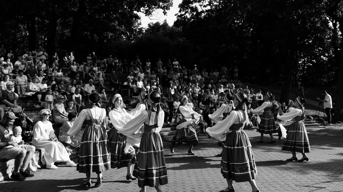 Black and white photo of dancers in traditional attire performing in front of an audience outdoors.